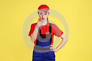 Confident worker woman standing, raising finger, showing warning gesture, looking at camera.