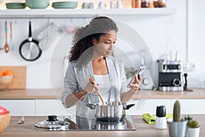 Confident young african american woman healthy food while using her mobile phone in the kitchen at home