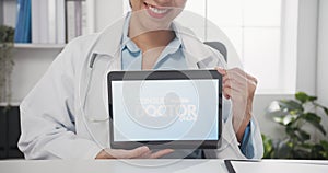 Confident young Asia female doctor in white medical uniform with stethoscope looking at camera and showing digital tablet in