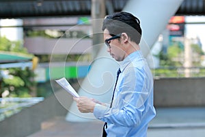 Confident young Asian business man looking paperwork or charts in his hands between go to the office