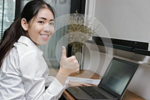 Confident young Asian business woman showing thump up hand sign on office.