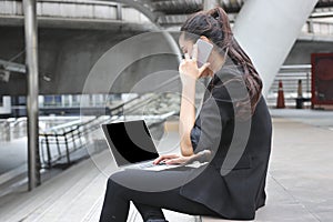 Confident young Asian business woman using laptop and mobile smart phone for job at outside office