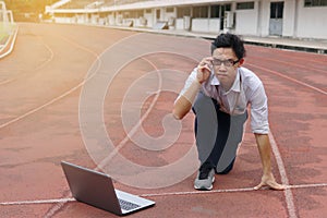 Confident young Asian businessman with laptop ready start position to forward on race track with sunshine effect. Competition and