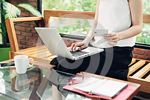 Confident young asian woman in smart casual wear working on laptop while sitting near window in creative office or cafe