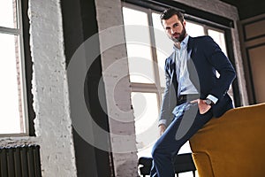 Confident young bearded brunet in elegant suit is looking at camera