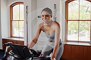 Confident young biracial woman doing cardio workout on exercise bike at the gym