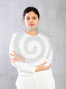 Confident young brunette standing with arms crossed on gray background