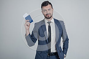 Confident young business man in classic black suit, shirt hold passport, boarding pass ticket isolated on grey wall background in