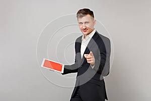 Confident young business man in classic suit pointing index finger on camera holding tablet pc computer with blank empty