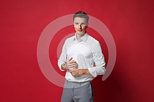 Confident young business man in white shirt, gray pants posing isolated on bright red wall background studio portrait