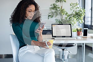 Confident young business woman sending messages with mobile phone sitting in the office