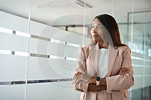 Confident young business woman standing arms crossed in office looking away.