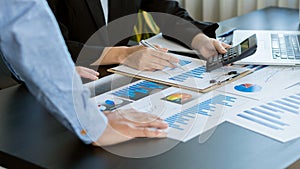 A confident young businessman analyzes graph data and calculates with a calculator and uses a computer while in the office.