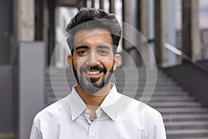 Confident young businessman with a beard smiling outdoors, modern professional in a white shirt