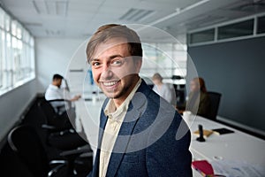 Confident young businessman in businesswear with next to desk with coworkers in office