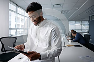 Confident young businessman in businesswear smiling and using digital tablet in office