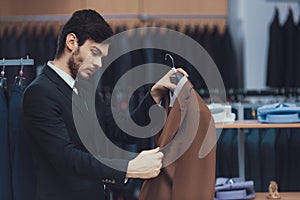 Confident young businessman looks at jacket in business mens clothing store.