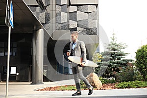 Confident young businessman walking on the street, using longboard.