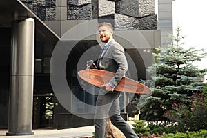 Confident young businessman walking on the street, using longboard.