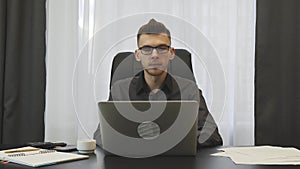 Confident young businessman works on laptop in office. Successful man in glasses working on computer at workplace. Male working on