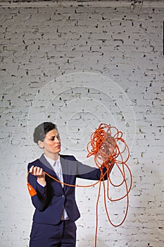 Confident young businesswoman looking at tangled red cable against white brick wall