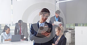 Confident young businesswoman using digital tablet with colleague at background in office