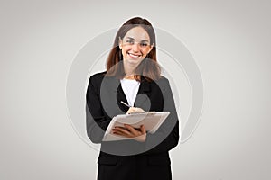 Confident young businesswoman with a warm smile writing on a digital tablet