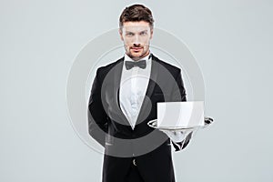 Confident young butler holding blank card on tray
