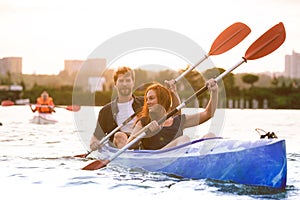 Confident young couple kayaking on river together with sunset on the background