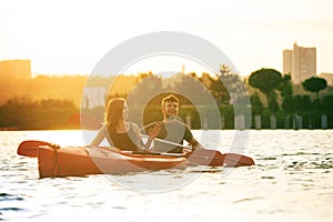 Confident young couple kayaking on river together with sunset on the background