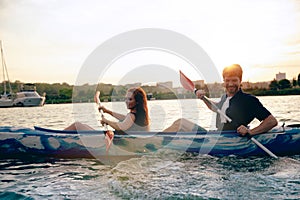 Confident young couple kayaking on river together with sunset on the background