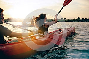 Confident young couple kayaking on river together with sunset on the background