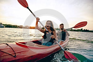 Confident young couple kayaking on river together with sunset on the background