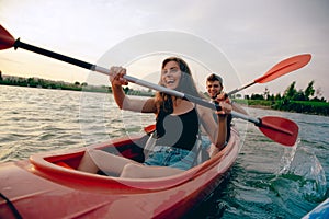 Confident young couple kayaking on river together with sunset on the background