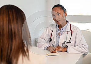 Confident young doctor writing down anamnesis of female patient