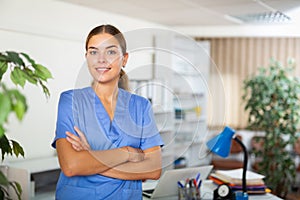 Confident young female doctor in blue uniform standing in office