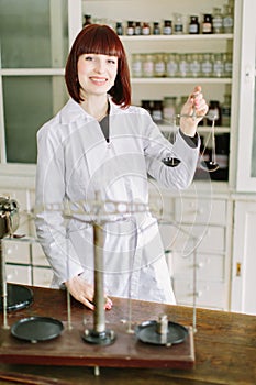 Confident young female pharmacist with a lovely friendly smile standing in the pharmacy and holding the scales in hands