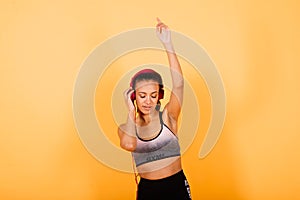 Confident young fit african sportswoman listening to music with headphones over yellow background