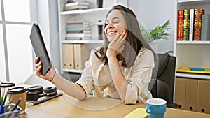 Confident young hispanic woman, a beautiful smiling business worker, enjoying success as she uses touchpad at her elegant office