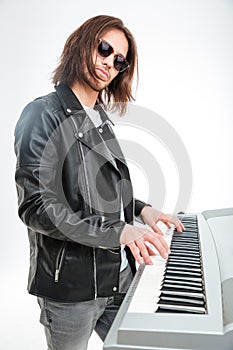 Confident young keyboardist in sunglasses standing and playing on synthesizer photo