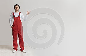 Confident young laborer in work uniform pointing aside at copy space
