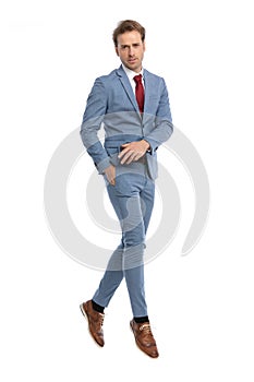 Confident young man in blue suit holding hand in pocket and jumping