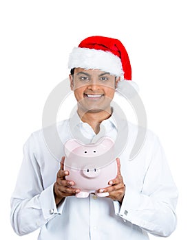 A confident young man in santa claus hat holding piggy bank