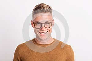 A confident young man in a studio, wearing glasses.