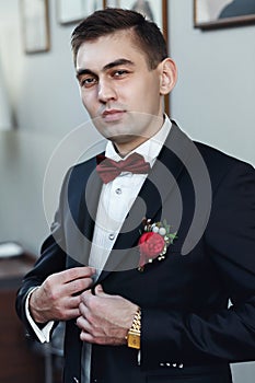 Confident young man in tuxedo with bow tie posing at camera hol