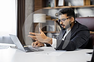 Confident young middle eastern businessman sitting at work table at modern office, speaking with customers