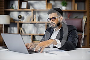 Confident young middle eastern businessman sitting at work table at modern office, speaking with customers