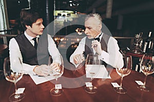 Confident young and old sommeliers discuss quality of wine drink in restaurant.