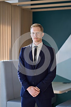 Confident young professional business man standing in office. Vertical portrait.