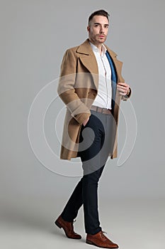 Confident young smartcasual guy in longcoat walking